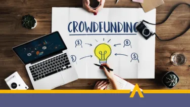 Plansza z napisem crowdfunding obok laptop i aparat