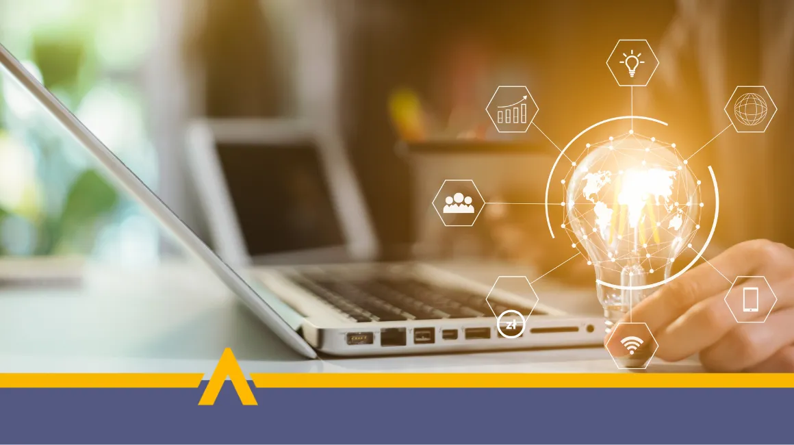 Osoba korzystająca z laptopa, trzymająca żarówkę z graficznymi ikonami technologii i finansów na tle