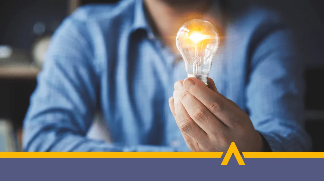 Mężczyzna w niebieskiej koszuli trzyma zapaloną żarówkę, symbolizującą pomysł, innowację lub rozwój biznesu.